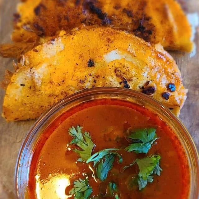 Licha's quesabirrias — tortillas dipped in chili sauce, filled with cheese and slow-cooked birria, served with a side of consommé